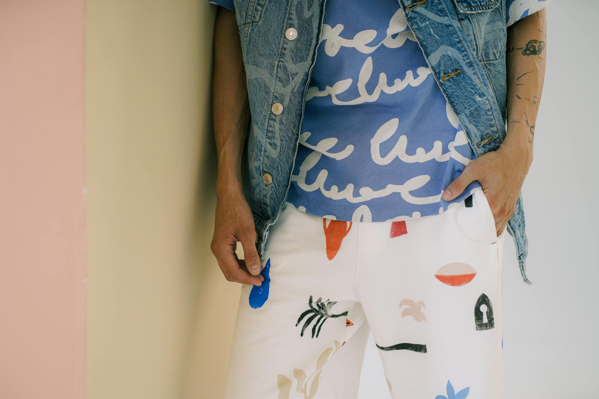 Close-up of a stylish outfit featuring a denim vest, blue graphic t-shirt, and patterned white pants.